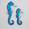 Two seahorse-shaped wall art pieces made of blue mosaic tiles with iridescent accents, displayed against a light gray background. Seahorse Wall Art, Affirmations & Hangings at World Of Decor NZ